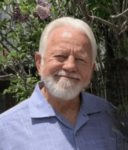 Smiling man outdoors near flowering bush.