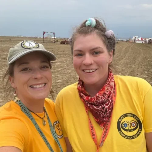Two women smiling outdoors in yellow shirts with badges.